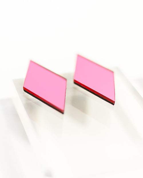 A pair of geometric stud earrings with bright pink faceted diamond-shaped tops and pink and black edges, displayed on a clean white surface.