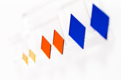 Close-up, shallow depth-of-field view of three pairs of acrylic geometric diamond earrings in blue, red, and golden yellow.