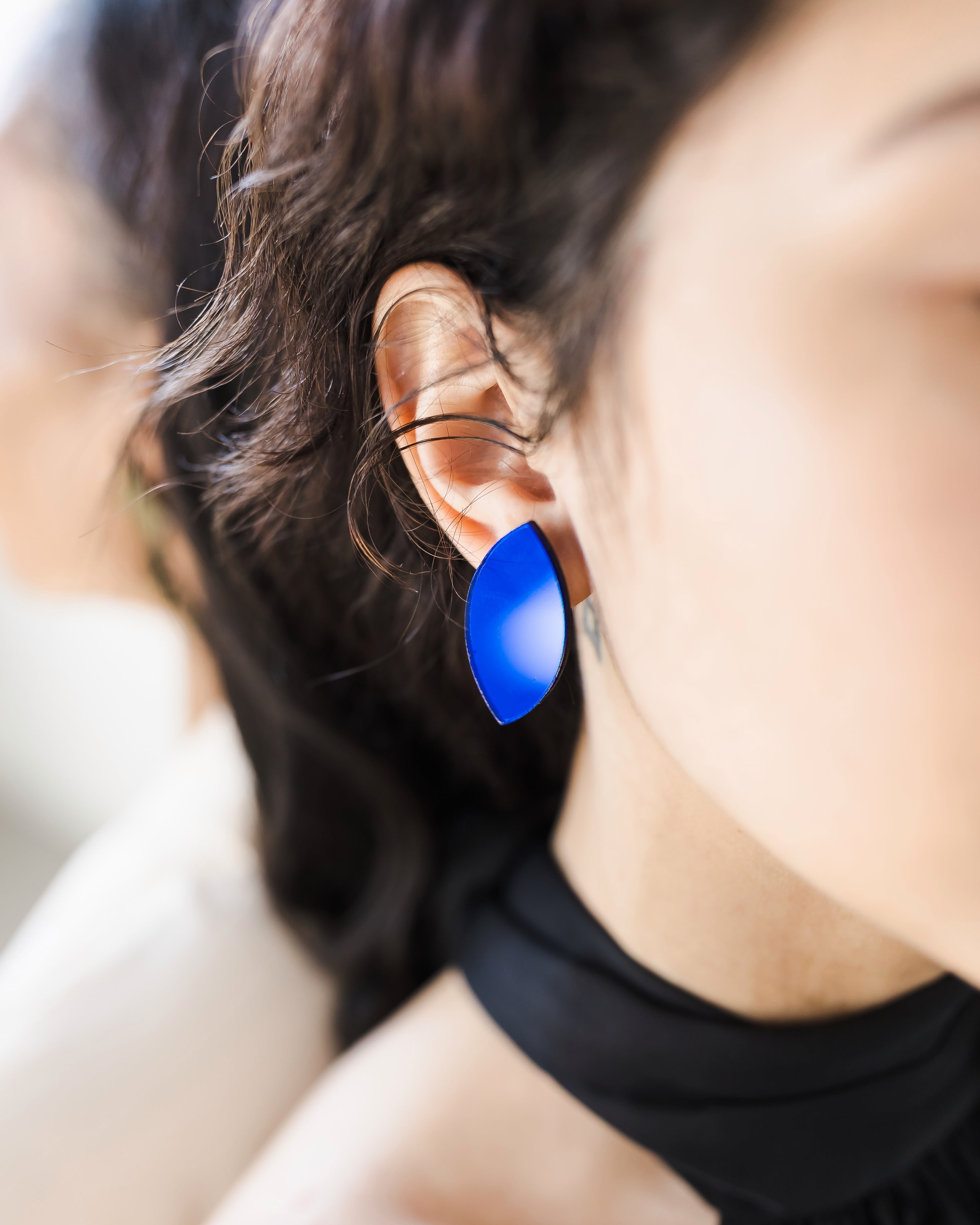 Woman out of view wearing reflective sapphire blue mirror acrylic earrings shaped like oval with two pointed ends.