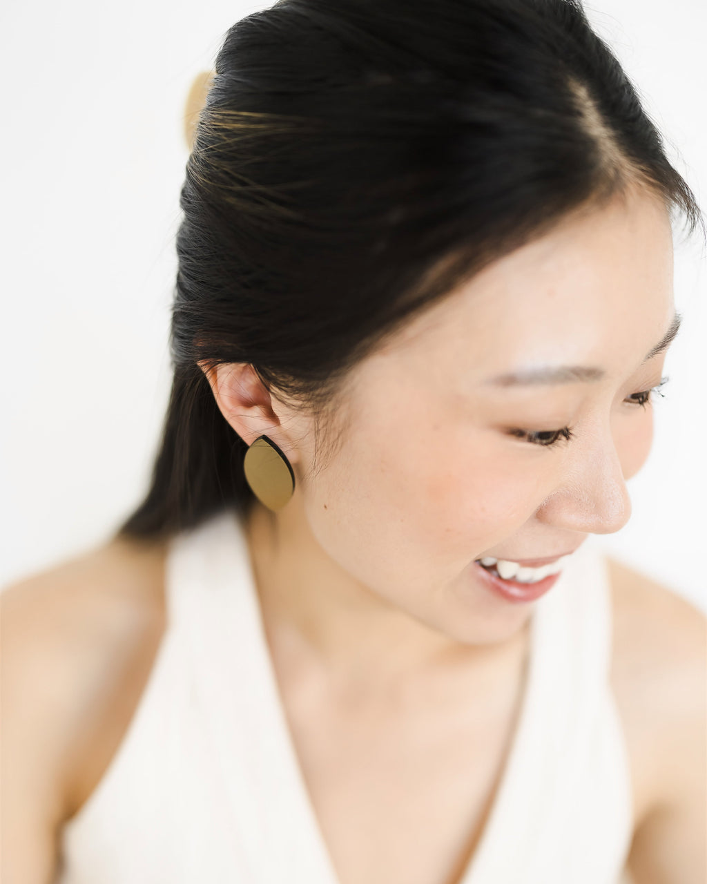 Woman wearing satin gold acrylic earrings with a plain background.