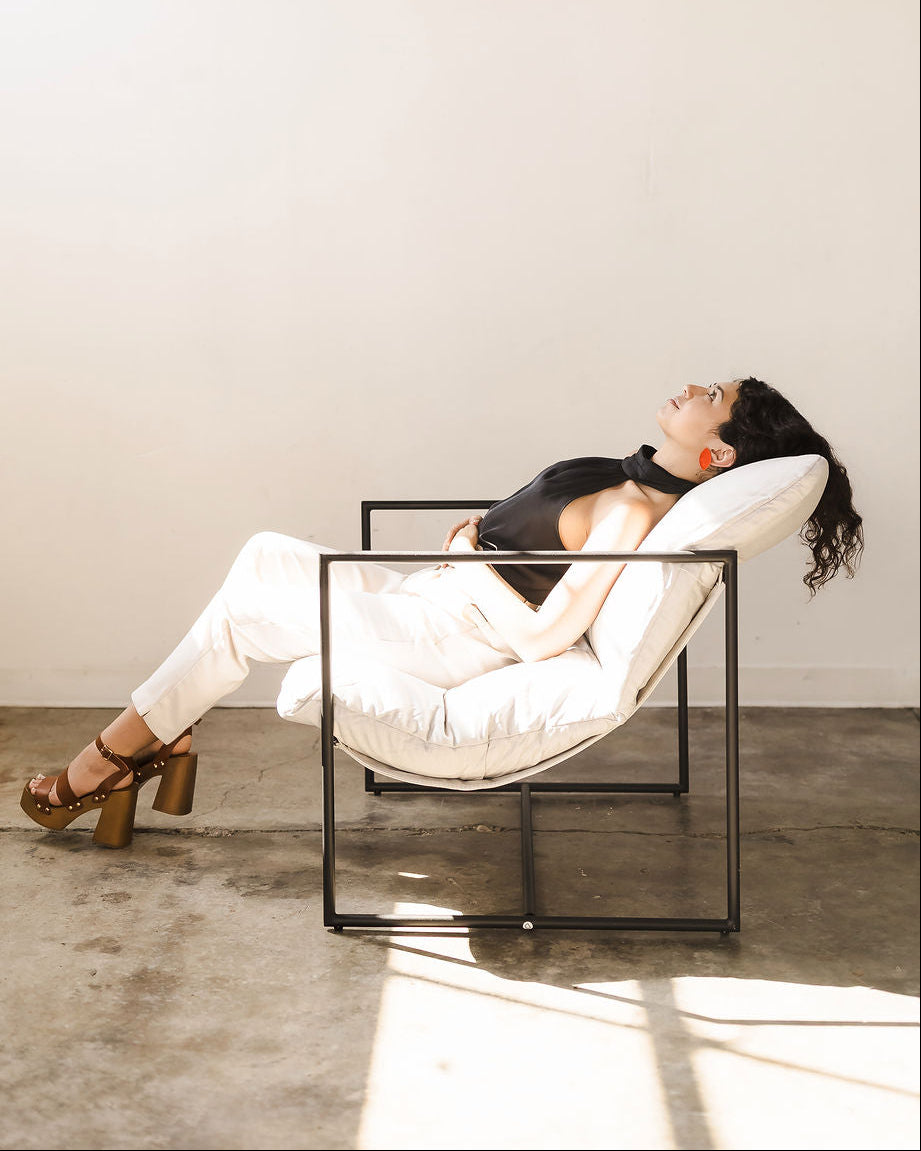 Woman relaxing in a modern white chair against a plain wall, wearing red earrings.