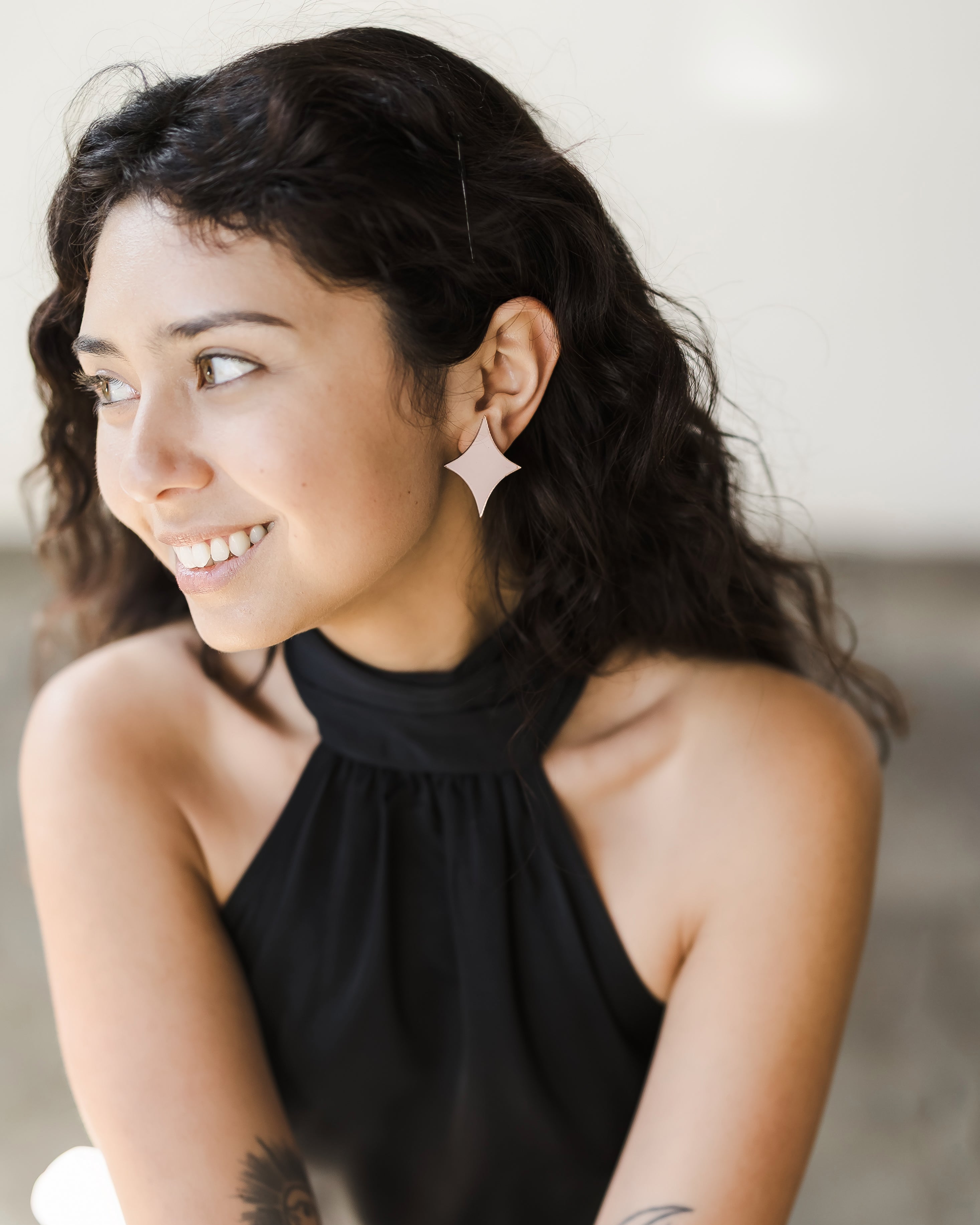 Young woman with long, curly hair wearing black sleeveless top and sparkle-shaped acrylic mirror earrings shaped like stars.