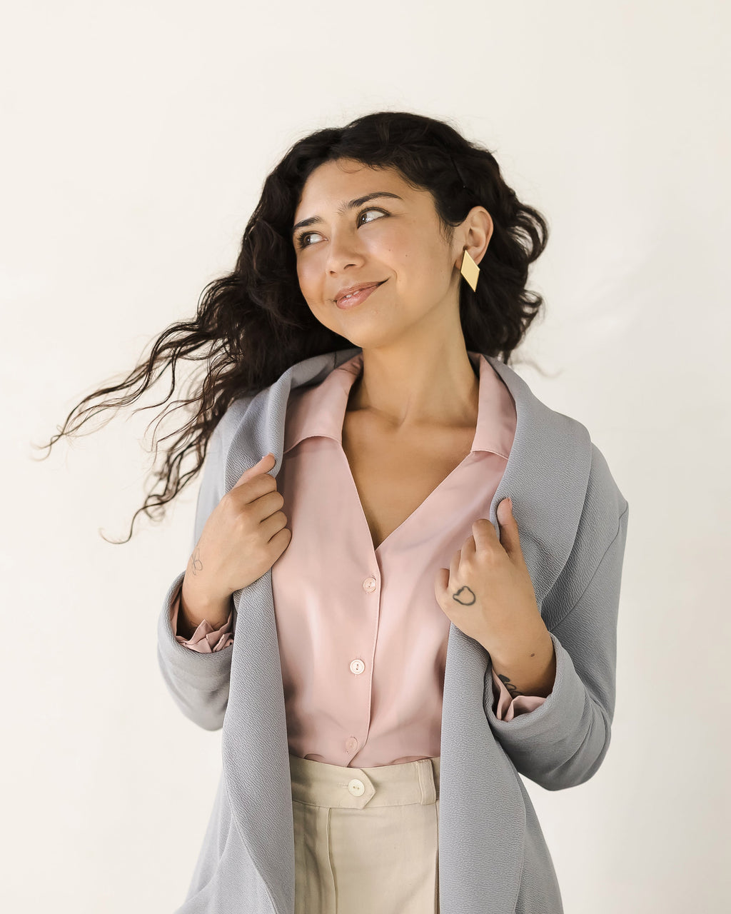 Woman wearing diamond-shaped mirror gold acrylic drop earrings, light gray blazer over a pink blouse with a white background.